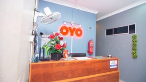 Un comptoir d’accueil avec un mur bleu, une grande enseigne « OYO », un ventilateur, une plante et un extincteur.