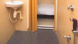 Une petite salle de bain avec un lavabo, une douche et un lit visible à travers une porte ouverte.