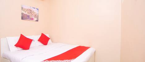 Una habitación de hotel con una cama, una colcha roja y blanca, y un cuadro en la pared.