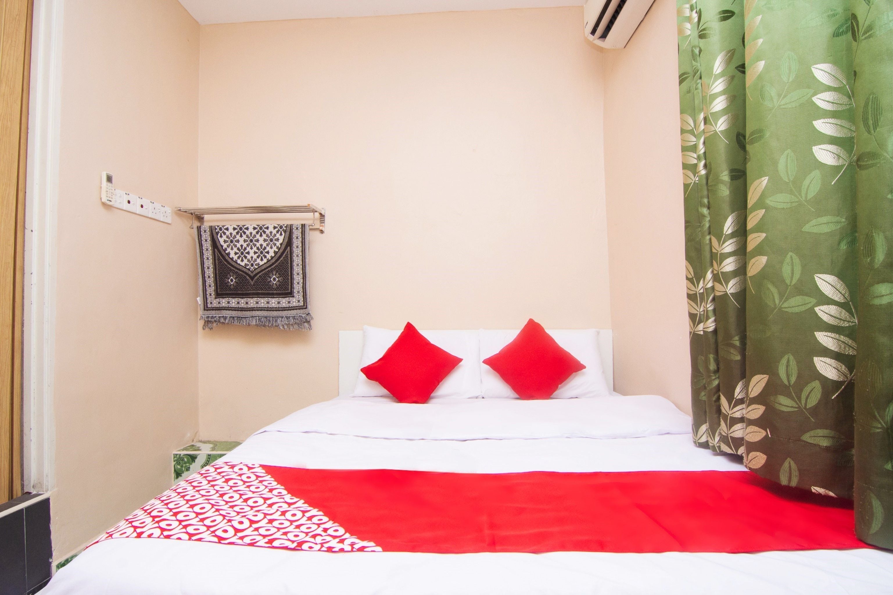Habitación de hotel con cama, un calefactor de pared, manta estampada y cortina verde.