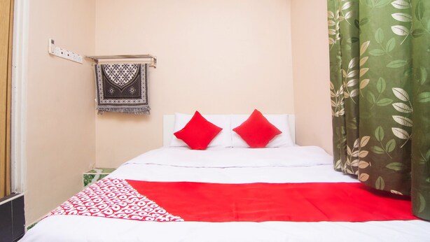 A hotel room with a bed, a wall-mounted heater, a patterned throw blanket, and a green curtain.