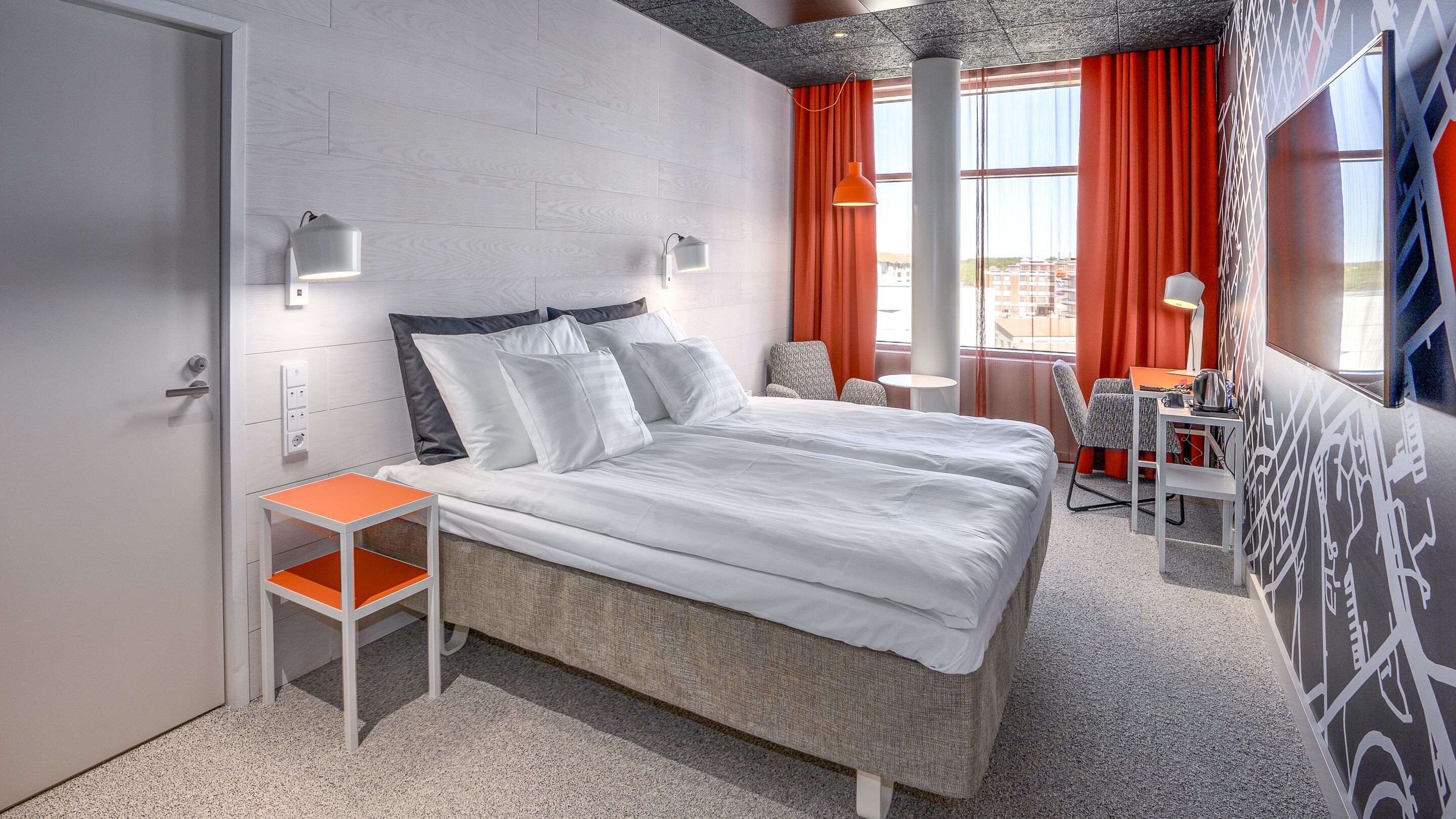 Ein modernes Hotelzimmer mit einem Bett, einem kleinen Tisch, einem Sessel und einem Schreibtisch mit Wasserkocher.