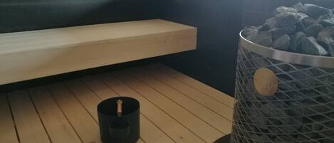 Una sala de sauna con un banco de madera, un cenicero negro y un cenicero metálico con carbón.