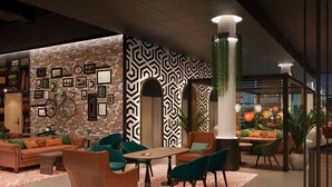 A modern lounge area with a brick wall, framed pictures, and a patterned wall. There are green and orange chairs, a wooden table, and a patterned rug. - Original Sokos Hotel Kupittaa (Turku)