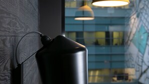 A black lamp with a coiled cord against a textured wall, with a modern building and hanging light fixture in the background. - Original Sokos Hotel Kupittaa (Turku)