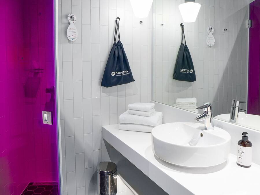 Casa de banho moderna com lavatório branco, duas luzes pendentes, um espelho grande e zona de duche com iluminação púrpura.