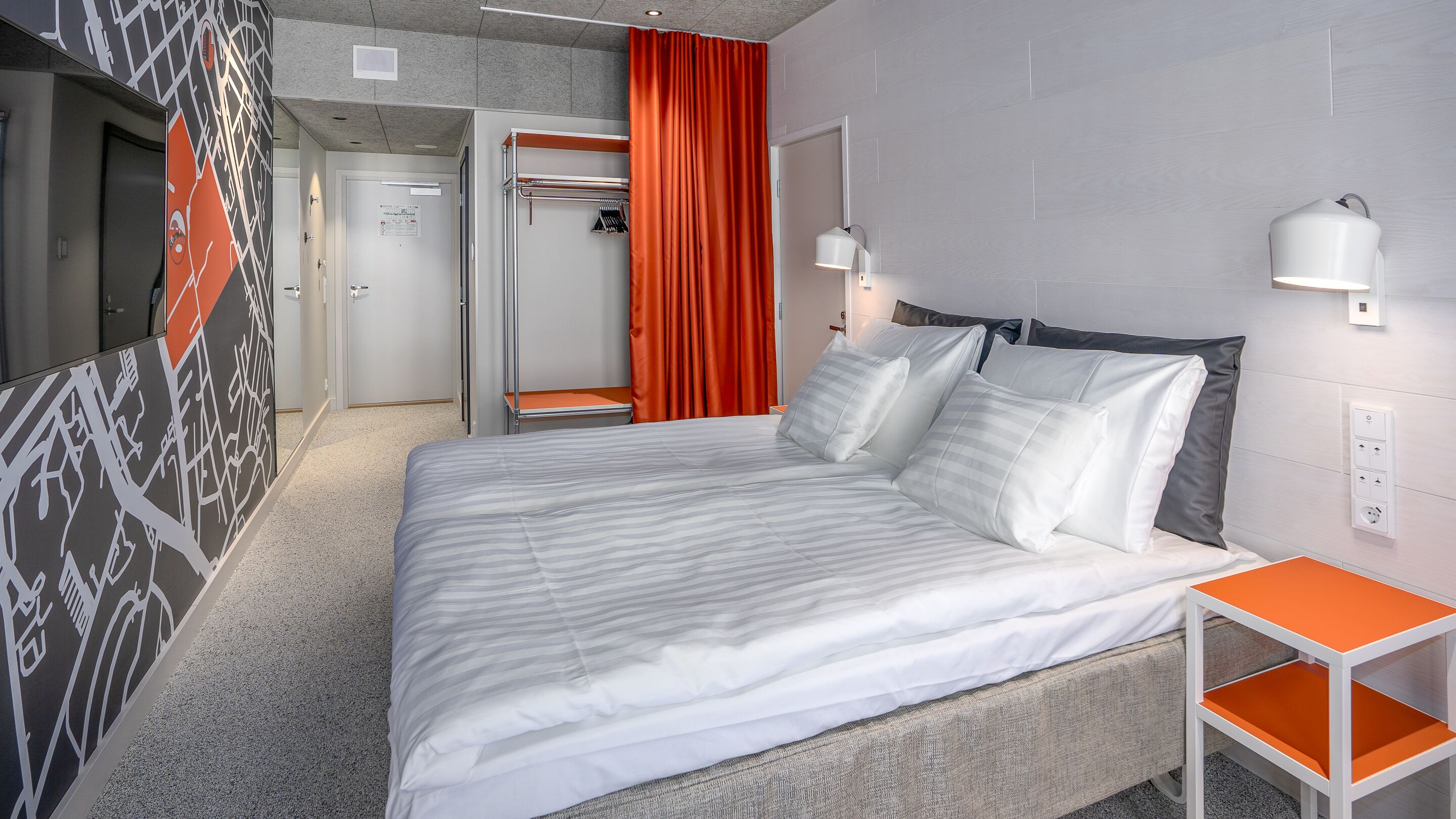 A modern hotel room with a large bed, a small table, and a wardrobe.
