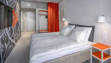 A modern hotel room with a large bed, a small table, and a wardrobe.
