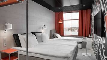 Habitación de hotel con dos camas, una mesita, un televisor y un ventanal con cortinas.