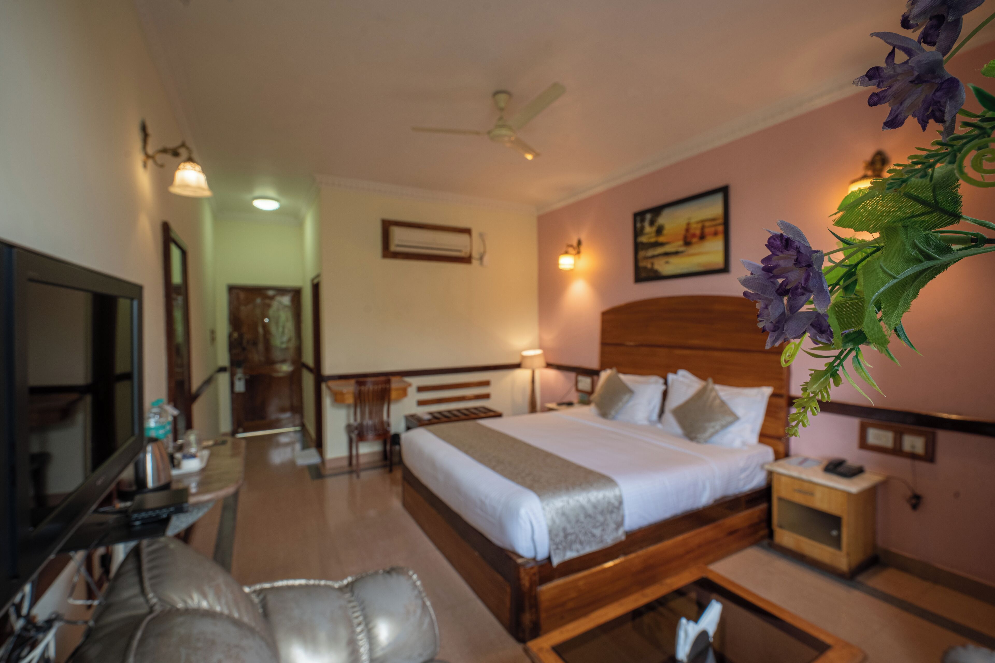 A hotel room with a bed, bedside table, lamp, and a decorative plant.