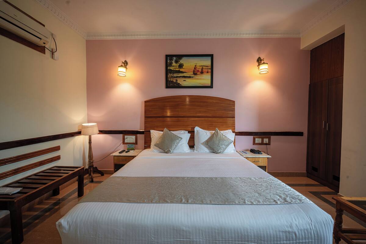 Hotellihuone, jossa on suuri sänky, kaksi yöpöytävalaisinta, puinen sängynpääty ja taulu seinällä.
