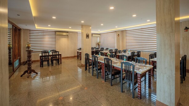 A spacious dining area with multiple tables and chairs, wooden paneling, and a polished floor. - Hotel Presidency (Bengaluru)