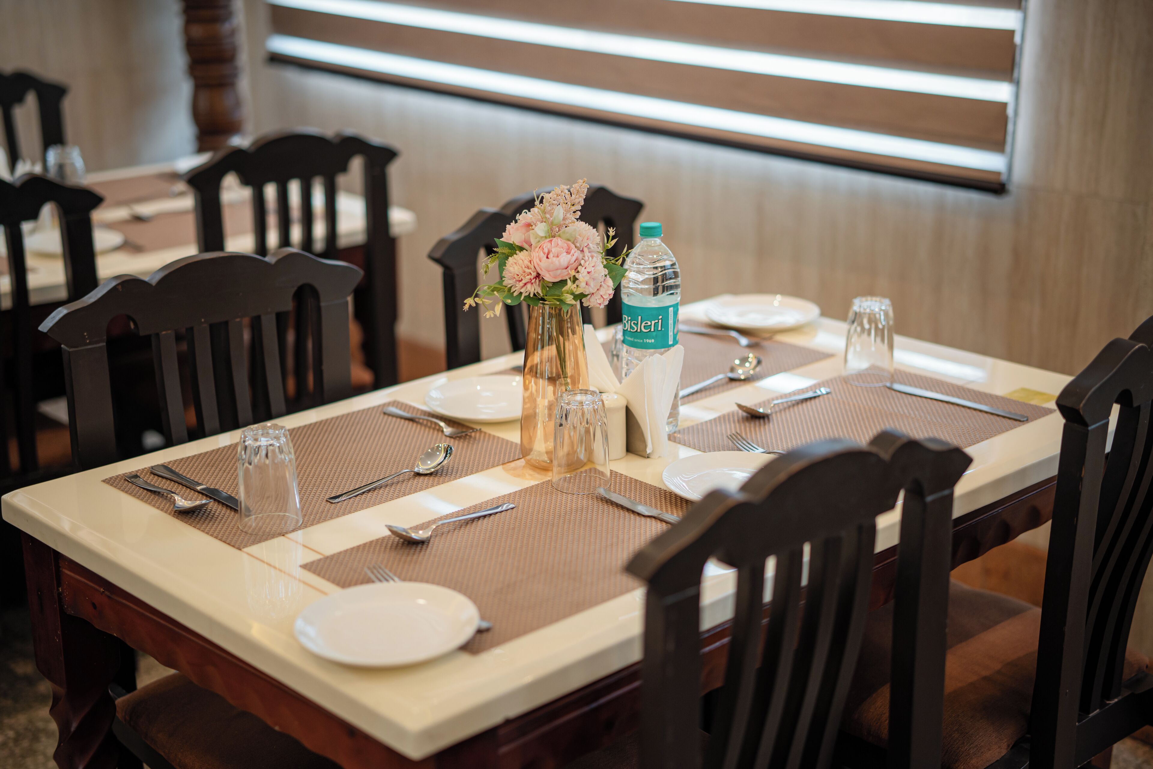 A dining table set with plates, cutlery, a vase with flowers, and a water bottle.