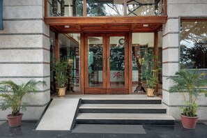 Entrada de un edificio con puerta de madera, plantas en macetas y escalones que conducen a ella.