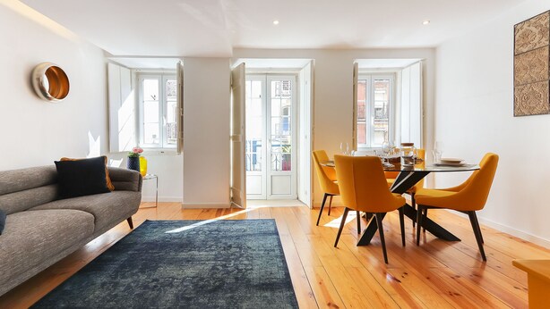 A modern living room with a sofa, a dining table with chairs, and a large window. - Cozy & Stylish central apt in XIX century building (Lisboa)