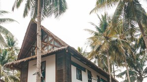 A two-story house with a thatched roof, surrounded by palm trees and a hammock. - Secret Spot Siargao - Hostel (General Luna)