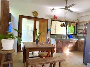A kitchen with wooden cabinets, a dining table, and a ceiling fan. - Secret Spot Siargao - Hostel (General Luna)