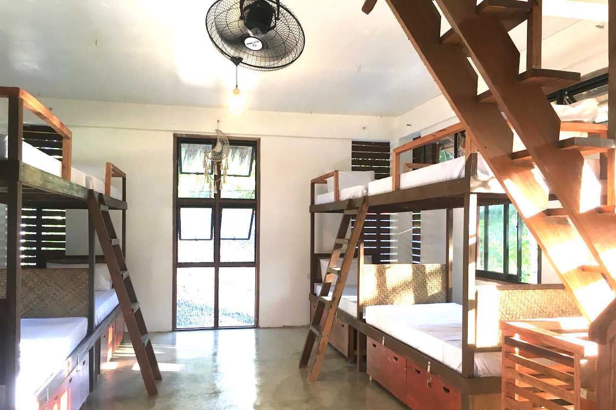 Quarto com beliches, ventilador e janela com persianas.