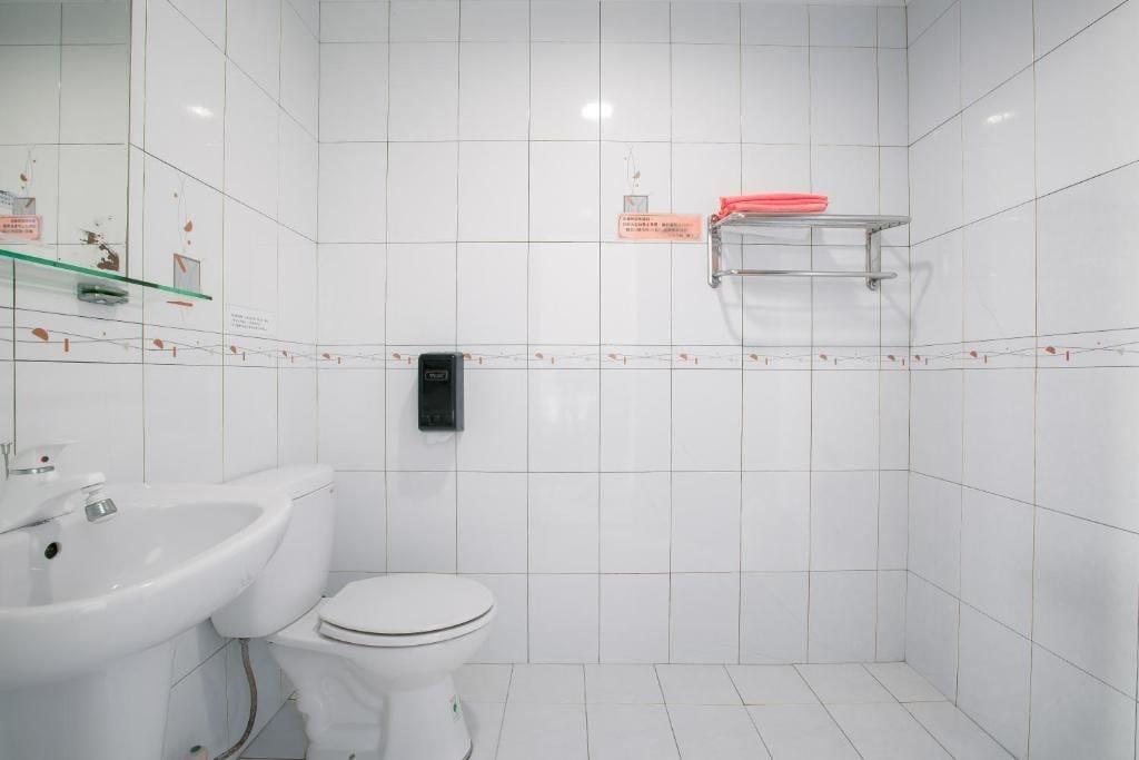 Un baño con azulejos blancos, un inodoro blanco, un lavabo y un dispensador de jabón.