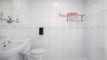 Un baño con azulejos blancos, un inodoro blanco, un lavabo y un dispensador de jabón.
