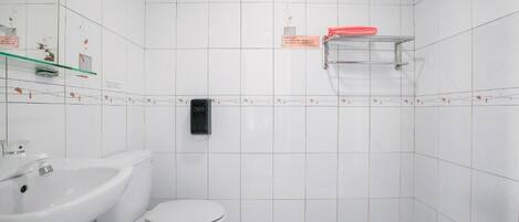 A bathroom with white tiles, a white toilet, a sink, and a soap dispenser.