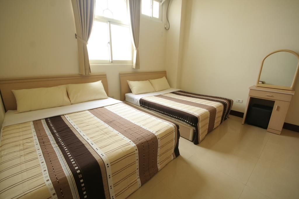 Una habitación de hotel con dos camas, un escritorio pequeño con un espejo y una ventana con cortinas.