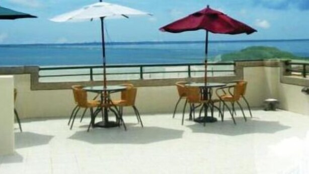 Een terras met twee tafels en stoelen, elk met een parasol, met uitzicht op een waterpartij.