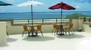 A terrace with two tables and chairs, each with a table umbrella, overlooking a body of water. - Long Beach Private Lodging (Magong)