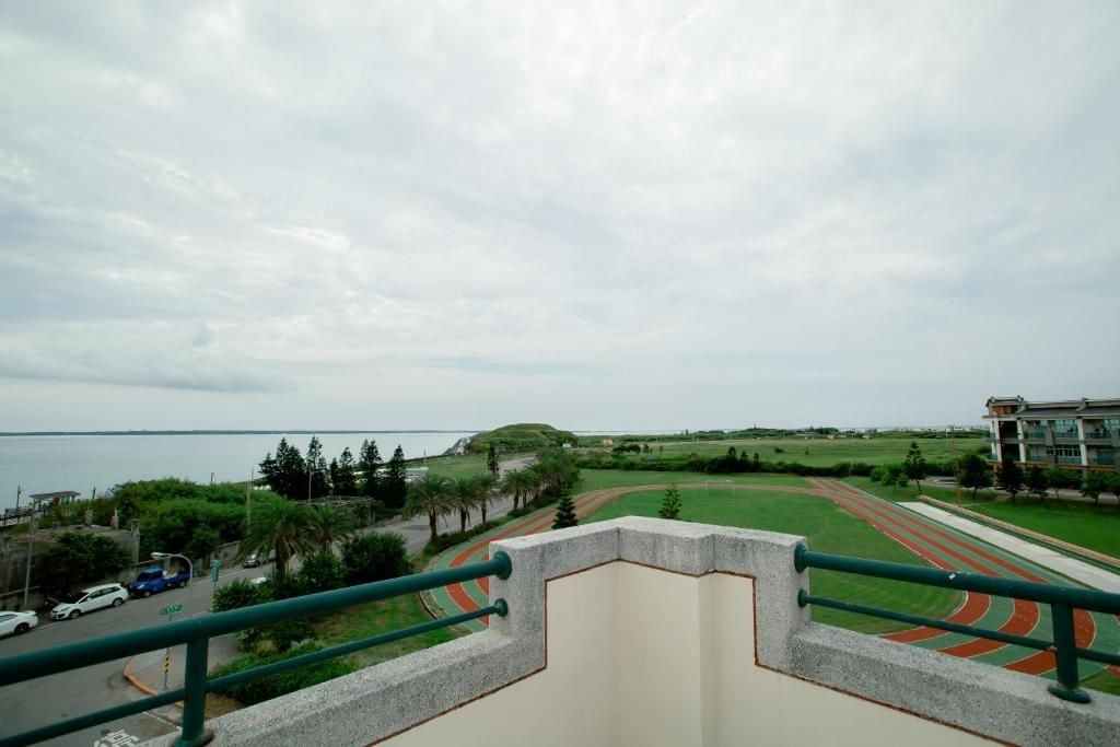 A view from a balcony overlooking a track field with a body of water in the background.