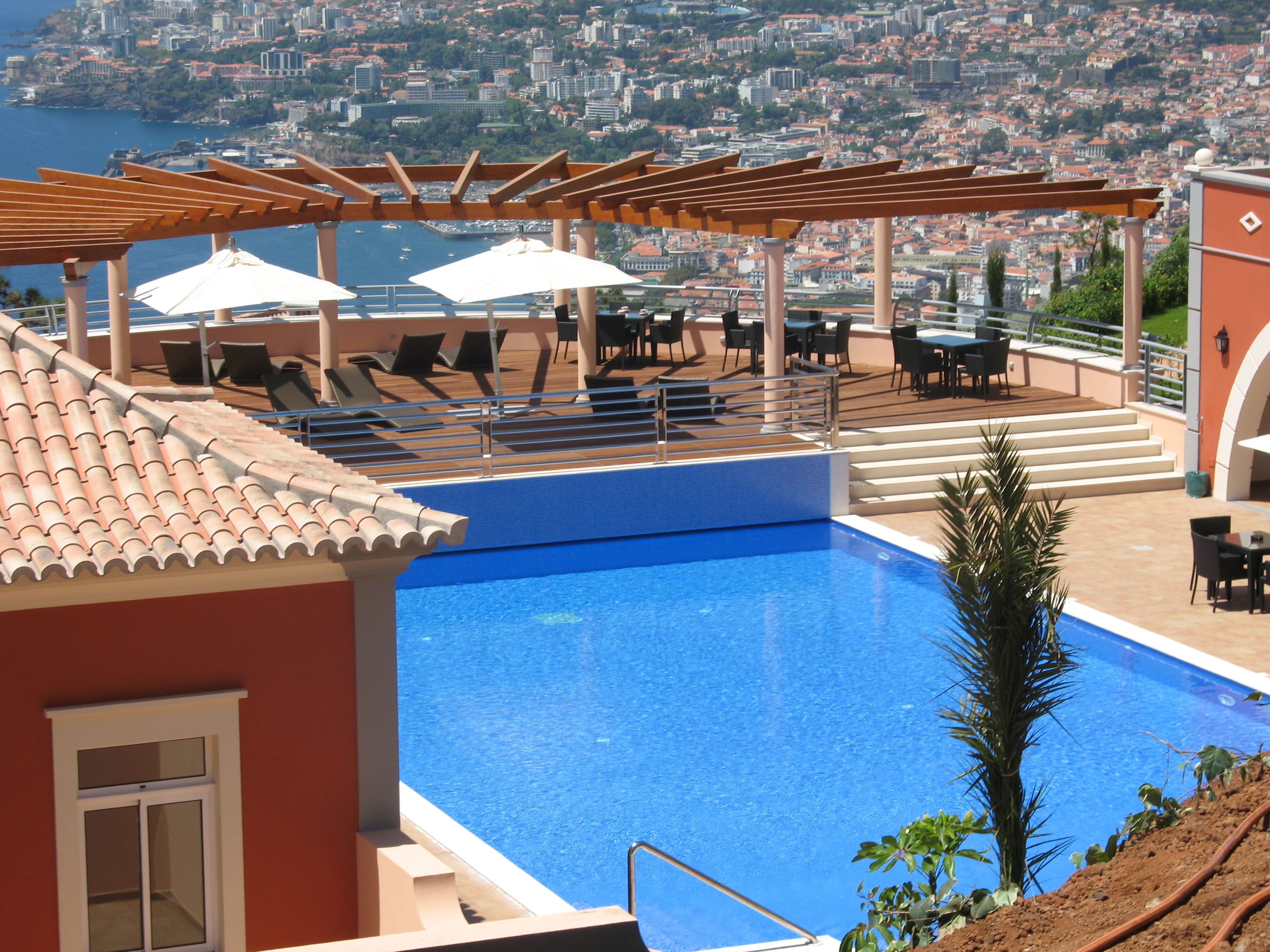Une piscine sur le toit avec vue sur la ville, des chaises longues, des parasols et un espace repas extérieur.