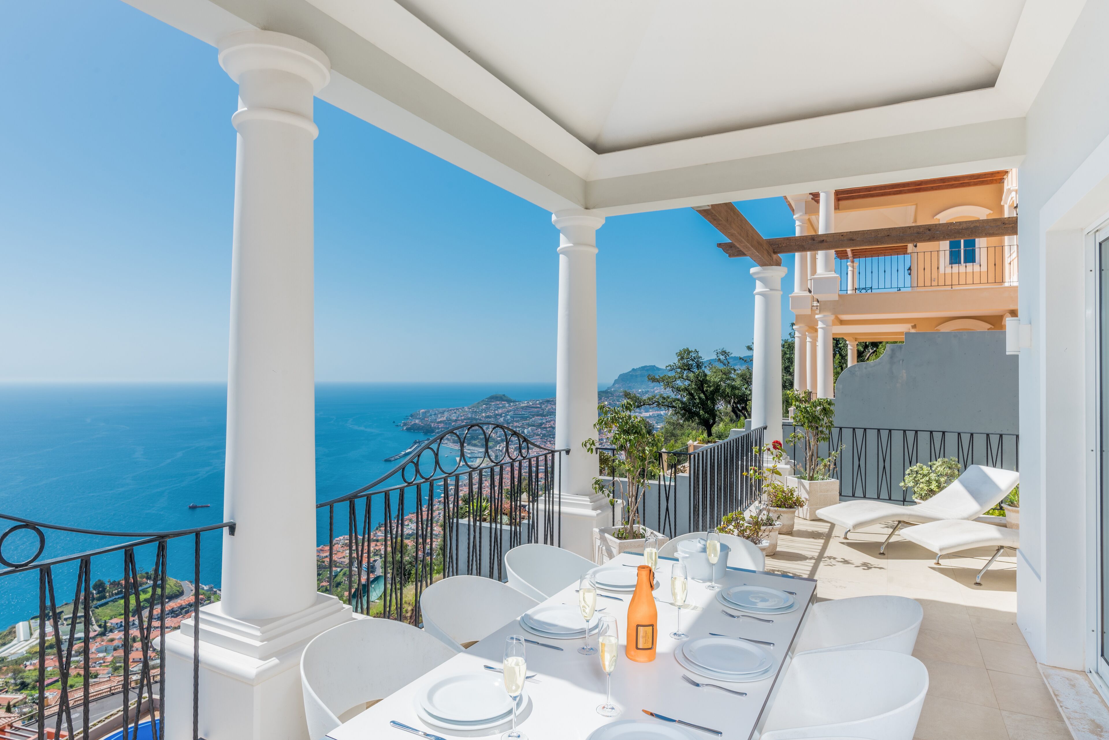 A terrace with a table set for dining, overlooking a coastal view.