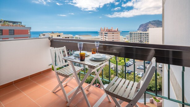 Un balcon avec une table dressée pour deux personnes, offrant une vue sur le paysage urbain et la mer.