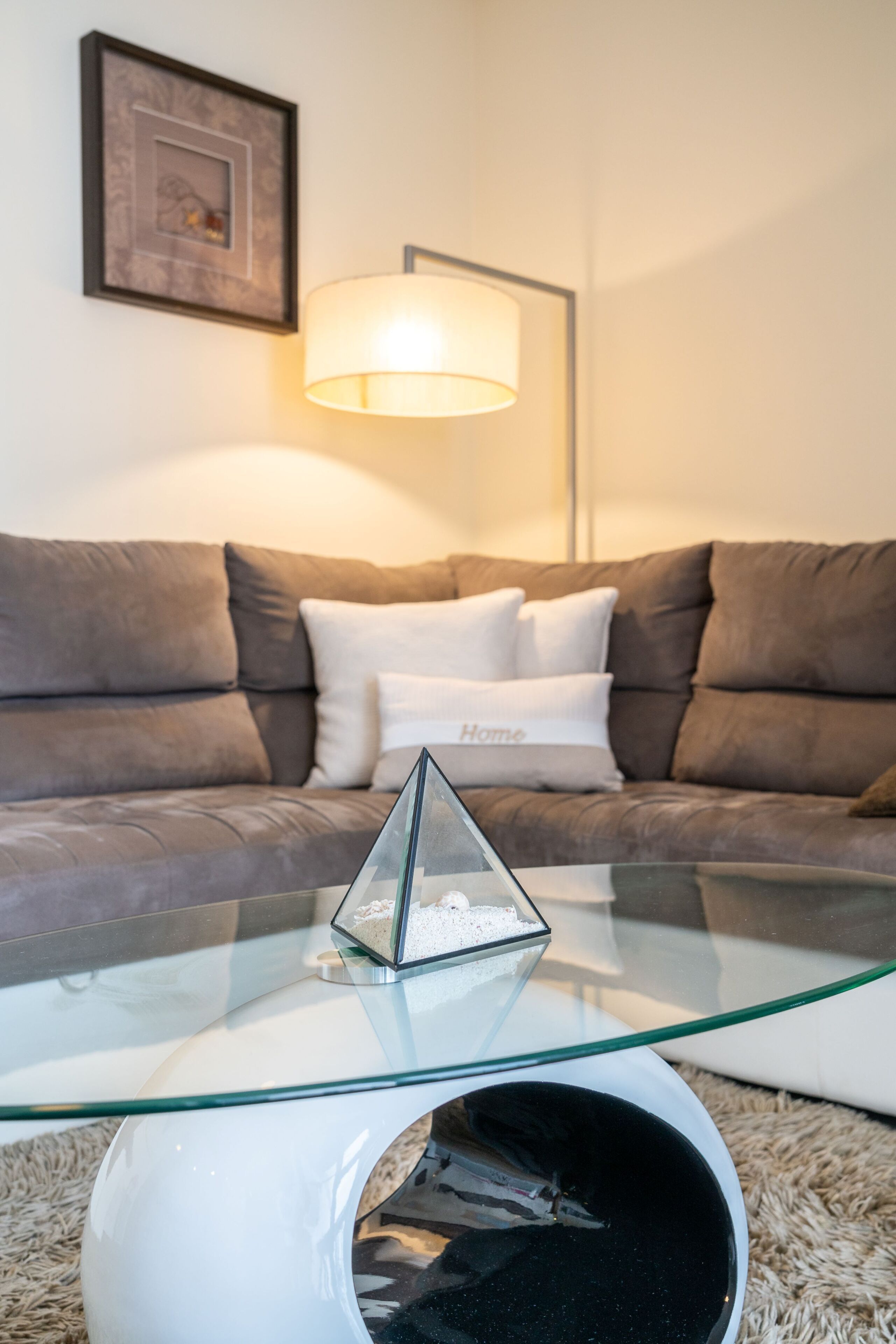 Ett vardagsrum med ett soffbord i glas, en soffa och en lampa.