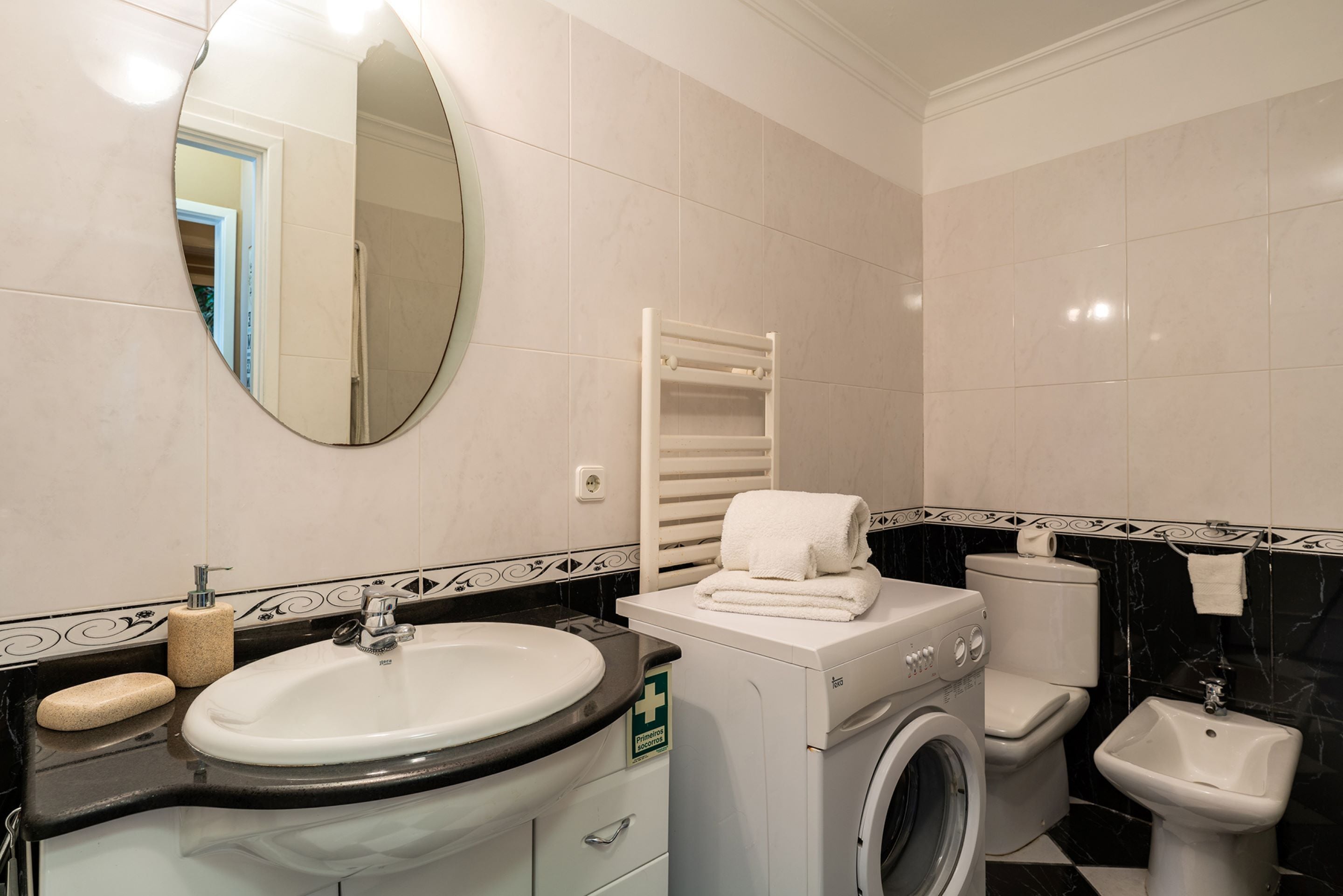 A bathroom with a sink, mirror, towel rack, toilet, and washing machine.