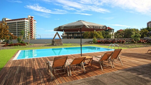 Une piscine avec une terrasse en bois, des chaises longues et un espace abrité avec un parasol.