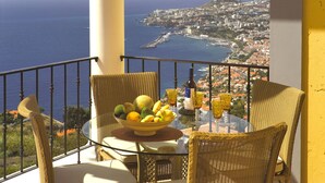 A balcony with wicker chairs, a glass table, and a bowl of fruit. - Dream Luxury Apartment  Palheiro Village (Funchal)