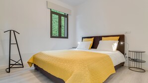 A neatly arranged bedroom with a bed, bedside table, and a standing lamp. - Lazareto Apartment (Funchal)