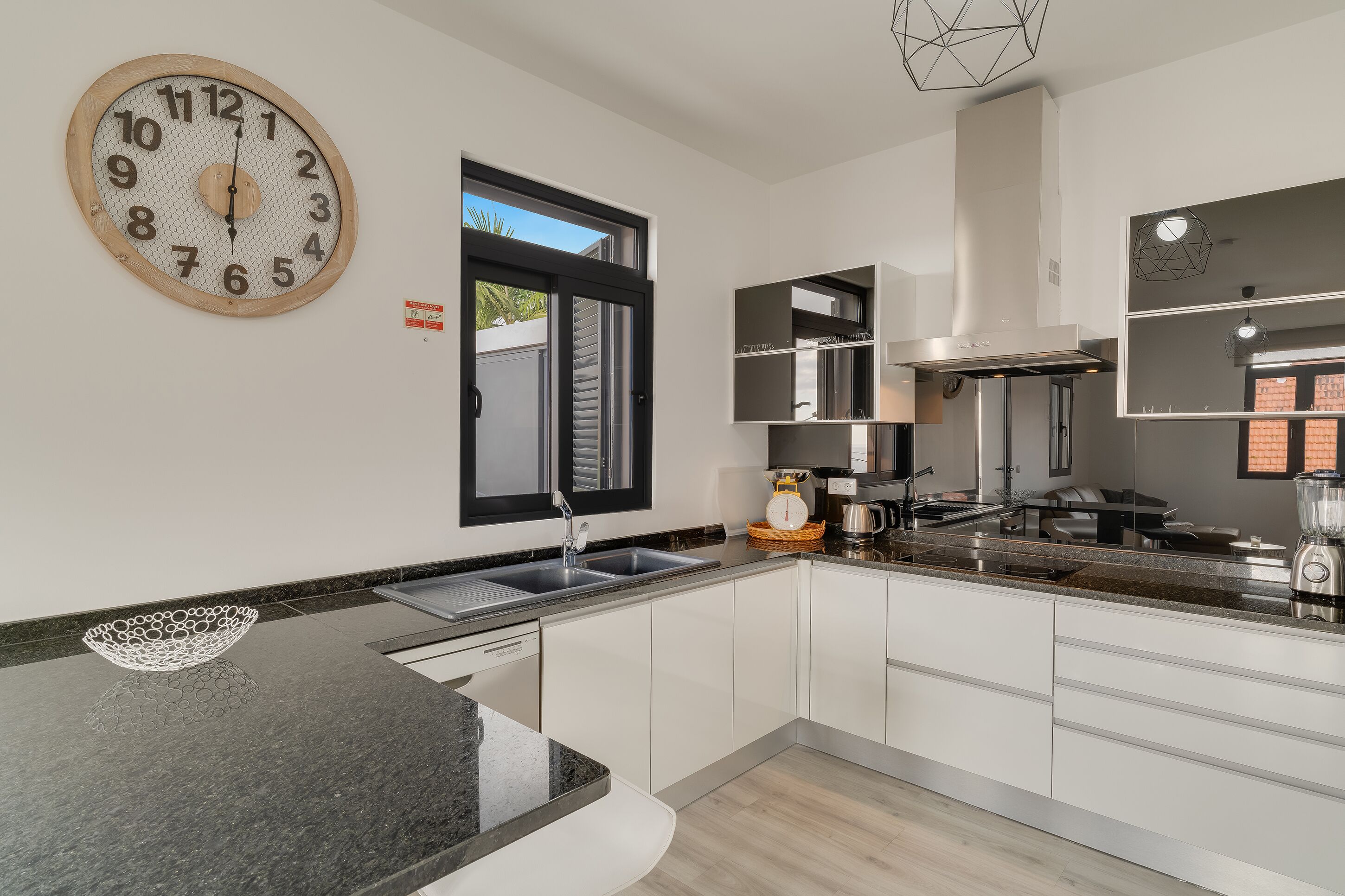 A modern kitchen with a large analog clock, a window, and a built-in oven.