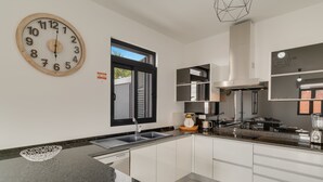 A modern kitchen with a large analog clock, a window, and a built-in oven. - Lazareto Apartment (Funchal)