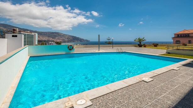 Ein rechteckiger Swimmingpool mit klarem, blauem Wasser, umgeben von einer gefliesten Terrasse.