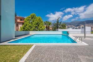 Ein rechteckiger Pool mit klarem, blauem Wasser, umgeben von einer gefliesten Terrasse und einer Rasenfläche.