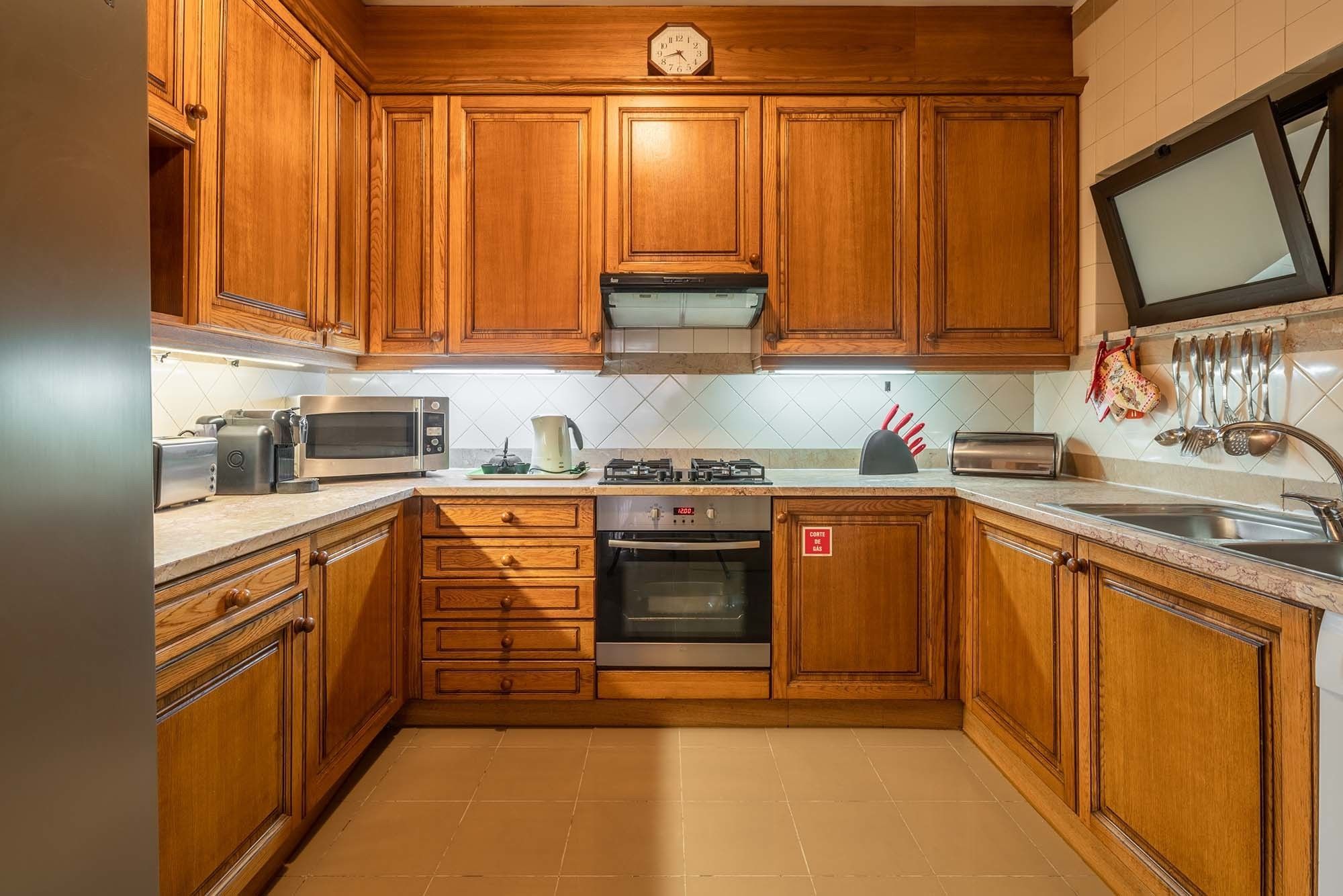 Una cocina con armarios de madera, un microondas, una estufa, un tostador y un reloj en la pared.