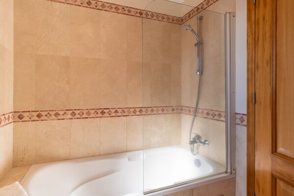 Une salle de bain avec une douche à parois de verre, une baignoire blanche et une porte en bois.