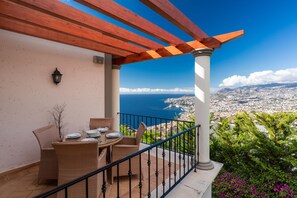 Un balcon doté de meubles en osier, d’une balustrade et offrant une vue sur une ville côtière.