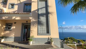 Un edificio a due piani con un'ampia finestra, piante in vaso e vista sul mare.