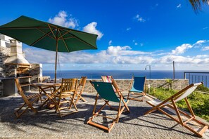 A terrace with wooden furniture, a green umbrella, and a view of the sea. - Villa Araújo da Costa (Santa Cruz)