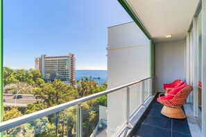 A balcony with a view of the sea, a high-rise building, and a red wicker chair. - Vista Savoy Apartment (Funchal)
