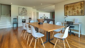 A spacious dining area with a wooden table and white chairs, a kitchen in the background, and a large anatomical poster on the wall. - Villa Nogueira IV (Funchal)