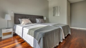 A double bed with a grey headboard, two bedside tables with lamps, and a grey throw blanket. - Villa Nogueira IV (Funchal)