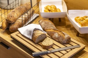Una tabla de madera con una hogaza de pan, un cuchillo y una cesta de cruasanes.